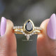 Two fingers holding the Black Pear Cut Moissanite Bridal Ring Set