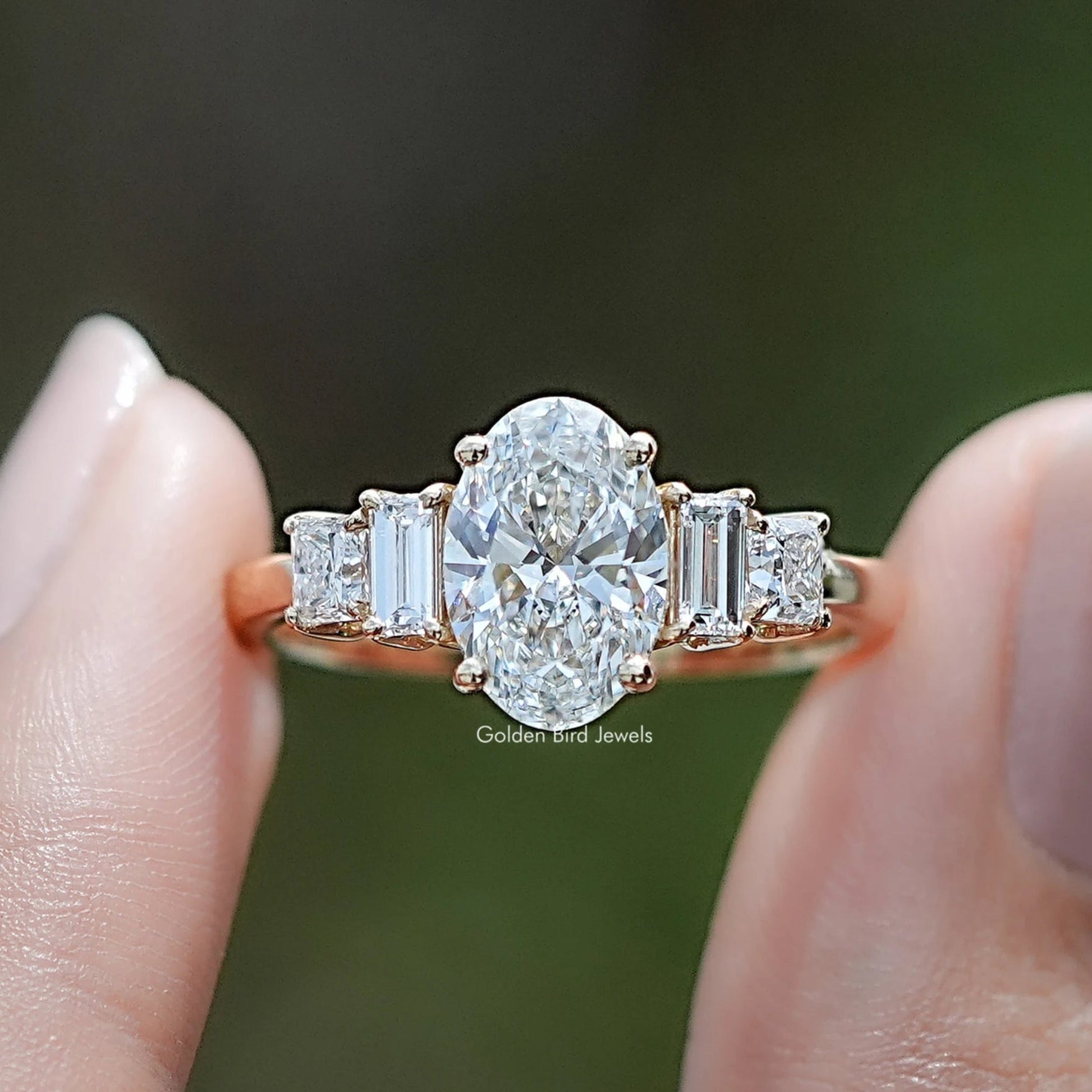 Oval Cut Lab Diamond Five Stone Engagement Ring BetweenTwo Fingers