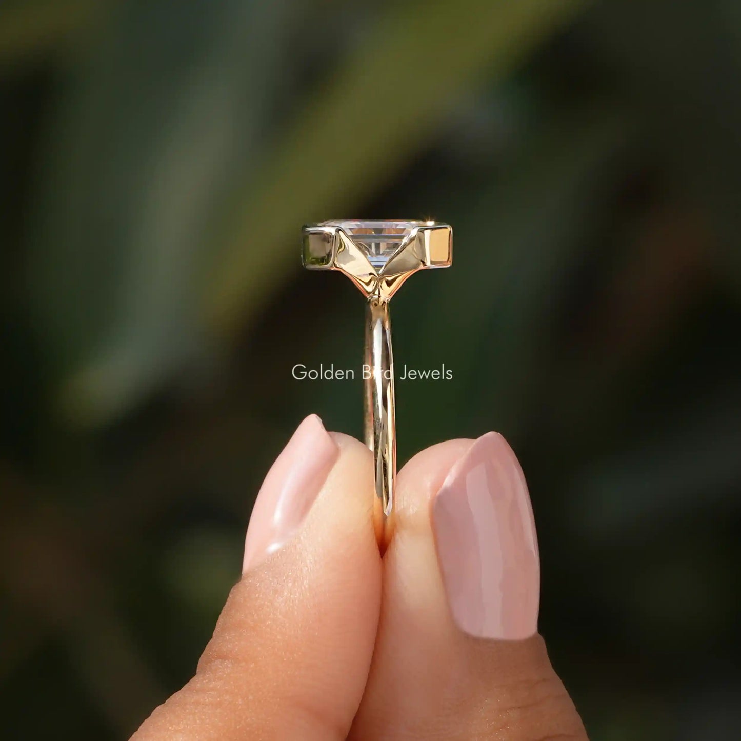 Side View of Emerald Cut Half Bezel Set Engagement Ring In two fingers